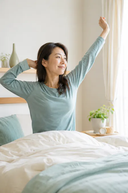 朝、ベッドで伸びをする女性